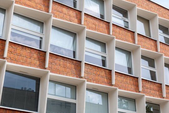 Modern red brick building facade with large windows in white frames, low angle upward view, geometric grid pattern, sky reflections, contemporary urban architecture exterior