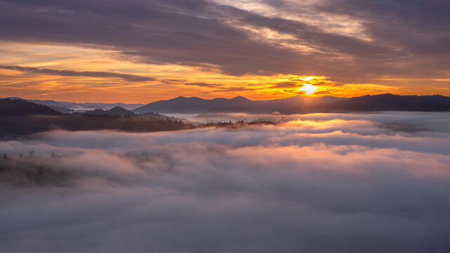 View of the sunrise over the rolling hills and dense fog covering the landscape in Moldovita, Suceava County, Romania.
