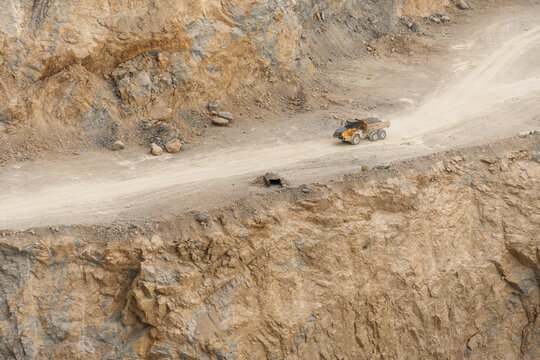 View of a yellow dump truck driving on a dirt road within a rocky quarry in the Apuseni Mountains, Horea, Alba County, Romania.