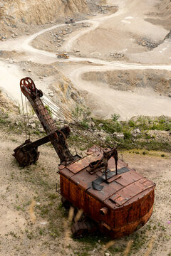 View of an abandoned, rusted mechanical shovel in a quarry in the Apuseni Mountains, with winding dirt roads and heavy machinery in the background, Horea, Alba County, Romania.