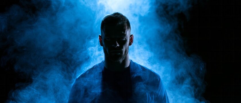 Cinematic low key silhouette of a man standing inside dense blue neon smoke or mist on a black background, sports or gaming advertising banner concept