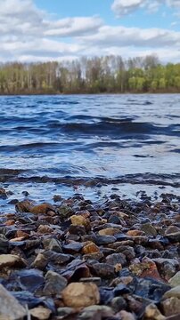 Rocky riverbank under cloudy sky. Scenic landscape, close-up of pebbles on the shore of a reservoir. Ecology, outdoor recreation and travel. Early autumn. View from ground level to the riverbank