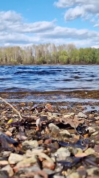Rocky riverbank under cloudy sky. Scenic landscape, close-up of pebbles on the shore of a reservoir. Ecology, outdoor recreation and travel. Early autumn. View from ground level to the riverbank