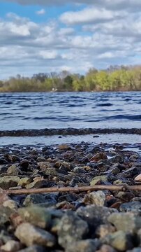 Nature landscape with rocky beach, clear water, waves and forest on the opposite bank. Ecology, outdoor recreation and travel concept. Early autumn. View from ground level to the riverbank