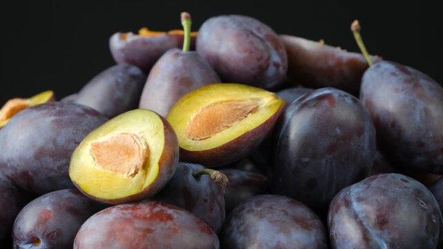 Fresh plum halves with pits on whole purple plums background video.