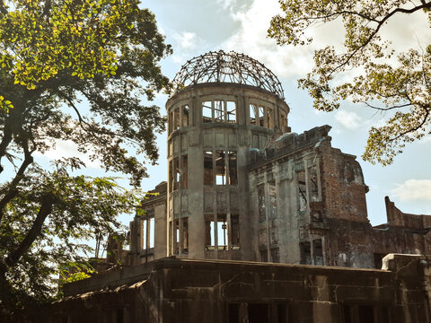 View of the historic Hiroshima Peace Memorial with its iconic exposed steel dome frame and weathered brick walls surrounded by lush green trees in Hiroshima, Hiroshima, Japan.