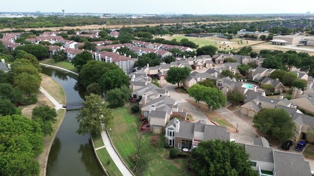 Aerial elevation captures sprawling canal system weaving through structured housing developments. Drone framing highlights lawns merging seamlessly with green parklands, Valley Ranch, Irving, TX