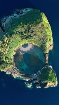 Circular crater lagoon in Azores near Sao Miguel, Portugal. Vertical overhead footage of Vila Franca do Campo Islet with shallow water inside volcanic crater
