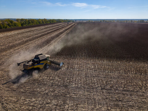 Agricultural combine harvests crop in expansive field, with dust trailing beside parallel rows of stubble. Sunflower is not identifiable in this view, which shows working machinery and rural farmland.