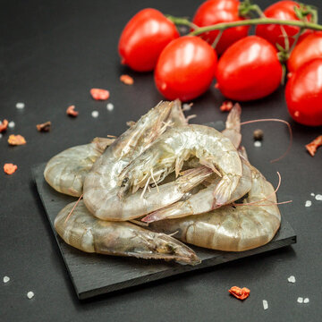Close up of raw king prawns on black slate plate with red tomatoes in background