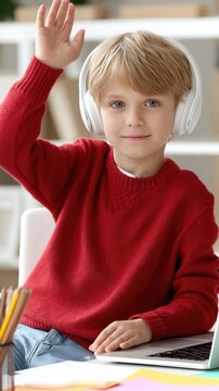 Young boy in a red sweater eagerly raises his hand while engaged in a study session at his cluttered desk filled with materials