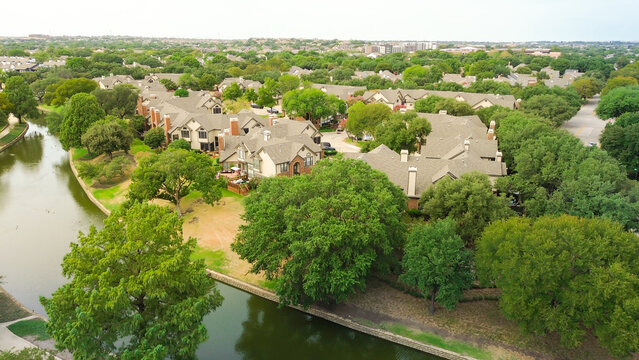 Waterway meanders through residential clusters within Valley Ranch neighborhood. Dense foliage surrounds multi-family housing units near paved walking paths bordering, Valley Ranch, Irving, TX