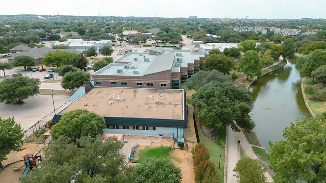 Commercial building sits adjacent to winding canal system within Valley Ranch. Flat rooftops overlook paved parking lots plus dense vegetation bordering, Valley Ranch, Irving, Texas