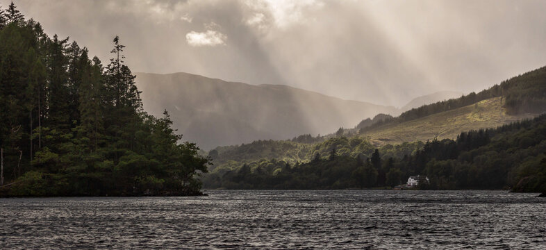 View of Loch Ard in Trossachs National Park, Scotland, surrounded by forest, sunrays through clouds