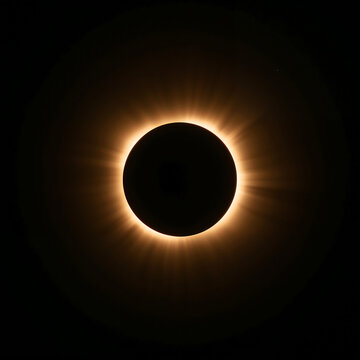 A total solar eclipse featuring a dark lunar disc surrounded by a warm golden glowing corona with intense light rays against a black background