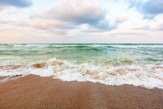 cloudy sunset above the green sea waters. waves crashing the sandy beach. clear horizon. changing windy weather. nature background