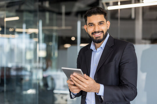 Young indian businessman smiling, holding tablet in modern office