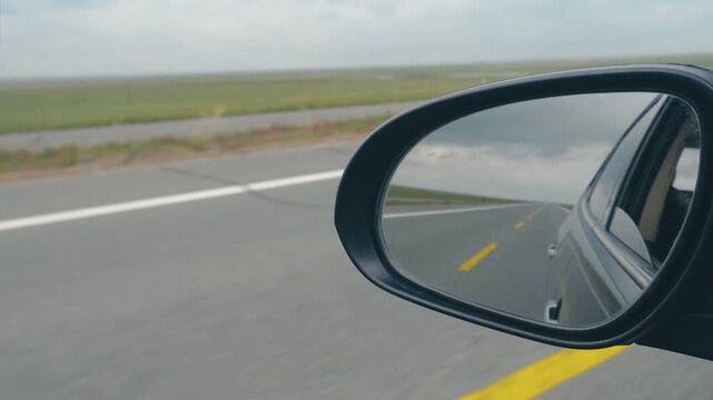 Side mirror view of a rural highway and road markings from a moving car