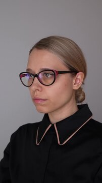 Young business woman puts on glasses in a studio portrait, demonstrating a tidy appearance and a strict professional business style
