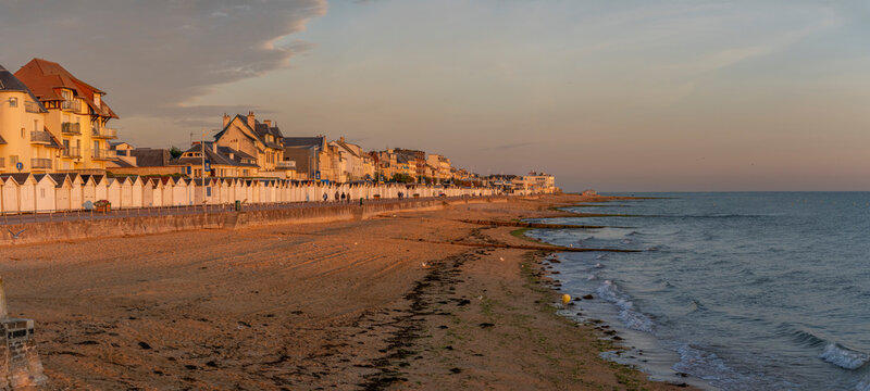 Luc-Sur-Mer, France - 08 08 2026: panoramic view wooden beach huts along the stone jetty, sand beach, sea and colorful sunrise sky behind