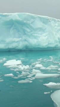 Vertical Video of Broken Ice Pieces Across Turquoise Water. Broken white ice spreads across blue-green water, showing varied frozen shapes, surface texture and gentle ripples in a natural seascape.