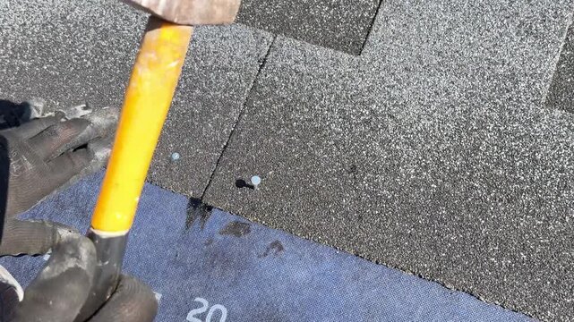 Hammering roofing nails into bitumen shingles during roof installation, home construction process