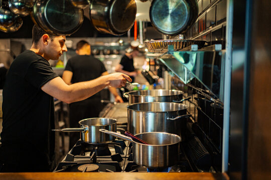 Chef preparing a meal on a commercial stove with cooking pots in a restaurant kitchen