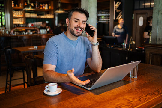 Smiling man on phone call using laptop in a coffee shop