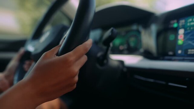 Close up of driver hands gripping steering wheel inside modern car cabin with glowing teal and cyan instruments and wide infotainment screen