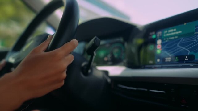 Two-hand grip on steering wheel inside modern car cabin with green instrument lighting and right-side navigation touchscreen map view in daylight from passenger seat angle