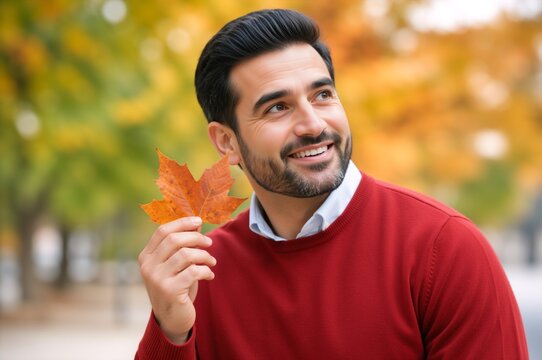 Happy man holding an autumn leaf in a colorful park. Smiling male outdoors enjoying fall season