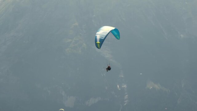 Tandem paragliding flight over a Swiss mountain village, Alps, Switzerland. Professional pilot and passenger flying above scenic alpine landscape. Adventure tourism, outdoor recreation and freedom.