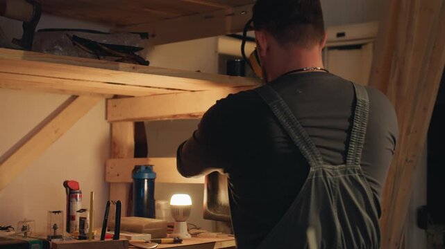 Man works in workshop handling wooden planks using tools like saws clamps measuring tape sandpaper hammers chisels drill. scene shows various woodworking materials and equipment