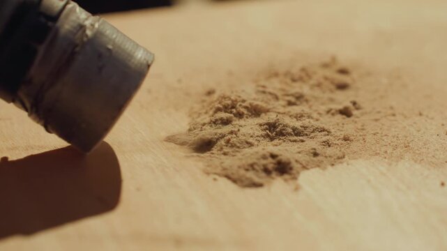 Close up perspective captures creation of woodwork details. hand held metal tool possibly drill or router actively produces fine sawdust on light colored wooden surface. focus remains