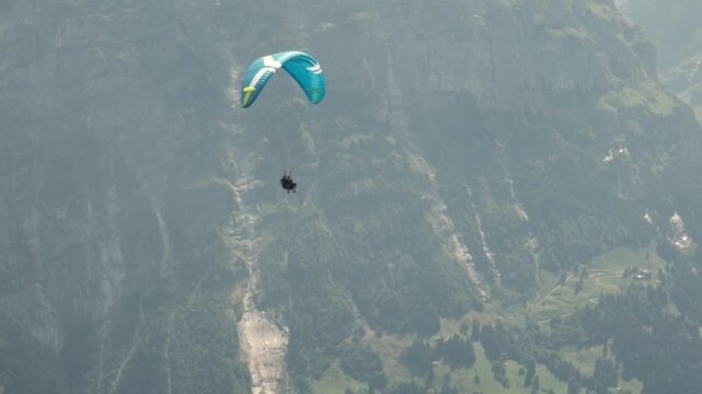 Tandem paragliding flight over a Swiss mountain village, Alps, Switzerland. Professional pilot and passenger flying above scenic alpine landscape. Adventure tourism, outdoor recreation and freedom.