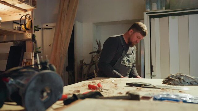 Carpenter inspects power equipment on active worksurface. Workshop details include scattered wood shavings hand tools like screwdrivers circular saw in use and protective gear such as ear