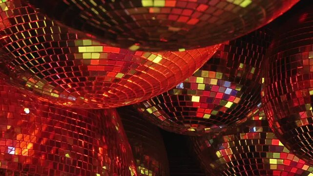 Close-Up of Disco Balls Reflecting Green and Gold Light. Tight framing emphasizes mirrored mosaic tiles and changing colored reflections across the rounded surfaces in a dark interior.