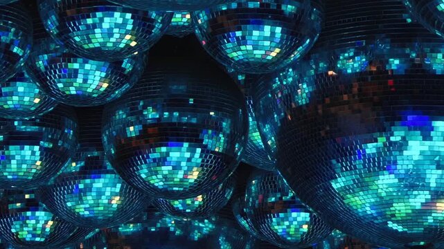 Clustered Mirror Balls Scatter Multicolored Light. The grouped mirror balls fill the frame as mirrored mosaic surfaces catch changing colored light and form an abstract pattern.