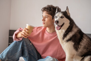Young owner sitting together with husky on wide bed, morning shared with northern breed, detail that turns ordinary hour into content. Wide shot. Concept of morning spent together with own dog © iwavephoto