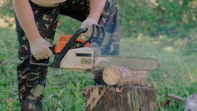 Worker using a chainsaw to cut a log on a tree stump outdoors, with sawdust flying during the cutting process in a grassy woodland setting