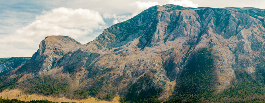 Dramatic Rocky Mountain Landscape with Forested Slopes and Cloudy Sky