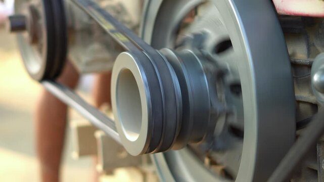 Mechanical Belt Drive System with Spinning Flywheel on Agricultural Diesel Engine. Rotating Engine Pulley with Rubber Drive Belt Transmitting Power Close Up Shot.