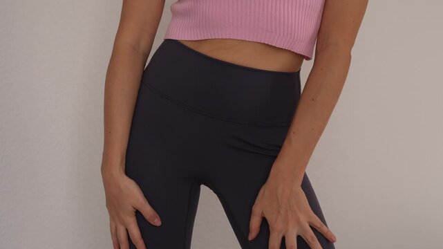 Young woman shows a toned figure and shaping leggings, touching hips and waist to highlight a slim body, activewear fit and a flattering silhouette at home