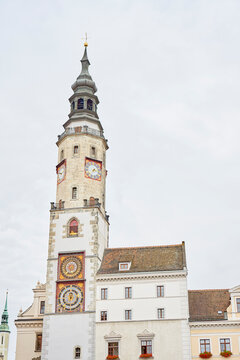 Historic clock tower with ornate clock faces, stone walls and tall spire above old buildings
