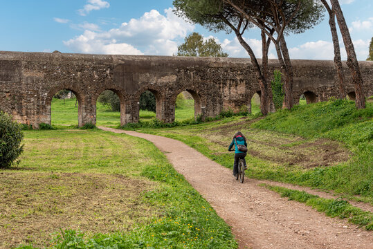 A Young Woman Cycling Along the Scenic Path Toward the Acqua Felice Aqueduct in the Parco degli Acquedotti, Rome