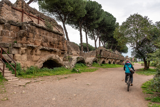 A Young Woman Cycling Along the Scenic Path Toward the Acqua Iulia Aqueduct in the Parco degli Acquedotti, Rome