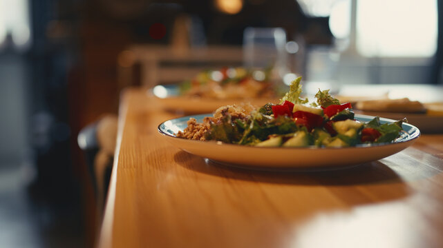 Close-up of a plate with buckwheat, fried onions, and fresh vegetable salad, bell peppers, cucumbers, and greens served on a wooden kitchen table. Healthy homemade meal in a cozy warm home.