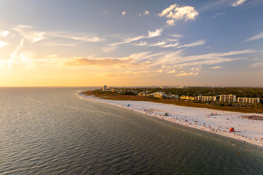 Crowded Siesta Key beach in Sarasota with clear blue water and soft sand, tourists swimming and relaxing under warm Florida sun at sunset.