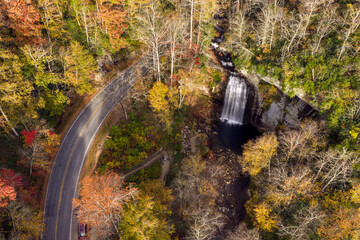Obraz premium Looking Glass Falls and Forest Heritage Scenic Byway from above during fall season. Scenic mountain road carries passing cars beside waterfall and observation platform in Pisgah National Forest.