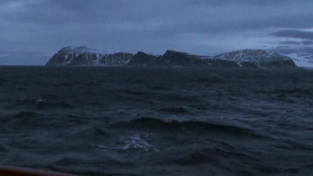 Cold Arctic Waters Moving Under Wide Polar Sky in Cold Northern Air. Dark swells move across the cold water while the distant polar horizon remains clearly visible.